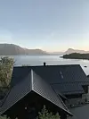 Bilde av hustak med fjord og fjell i bakgrunnen.