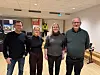 Fire personer står side om side i en konferansesal med faglige utstillingsstand bak.
