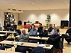 Personer sitter ved bord i konferansesal og lytter til en presentasjon.