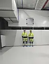 To personer i verneutstyr står i et teknisk rom med hvite vegger og ventilasjon i taket.