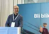 Mann ved talerstol foran blå bakvegg med teksten «Bli blikkenslager» og illustrert figur