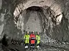 Tre anleggsarbeidere står i en nyutgravd tunnel med steinmasser bak seg