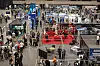 Innendørs fagmesse med mange stands, skjermer og besøkende i en stor hall.