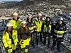 Gruppe arbeidere i gule verneklær på stillas med byen og åser i bakgrunnen
