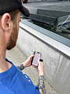 Mann med blå skjorte og caps bruker en smarttelefon ved et glassrekkverk.