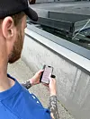 Mann med blå skjorte og caps bruker en smarttelefon ved et glassrekkverk.