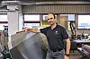 Jarle Kristiansen står i et verksted ved siden av en stor metallplate.