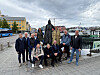 Gruppe mennesker poserer foran en statue ved en havnepromenade.