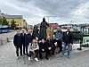 Gruppe mennesker poserer foran en statue ved en havnepromenade.