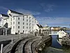 Hvit bygning ved en steinbrygge, med kanal, sjøhus og klar blå himmel.