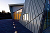 Moderne bygning med geometrisk fasade og opplyste vinduer ved skumring.