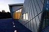 Moderne bygning med geometrisk fasade og opplyste vinduer ved skumring.