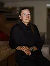 Kvinne i sort antrekk sitter i et varmt belyst interiør.
