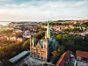 Historisk kirke med grønt spir omgitt av trær og tett bybebyggelse.