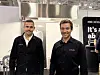 To menn poserer foran en utstillingsstand på en teknologimesse.