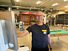 Arbeider i svart T-skjorte ved en industrimaskin i et verksted.